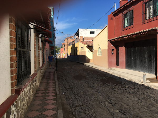 narrow
              cobblestoned street narrows to infinity in the far
              distance, shadowed by earth-tone homes under a deep blue
              sky