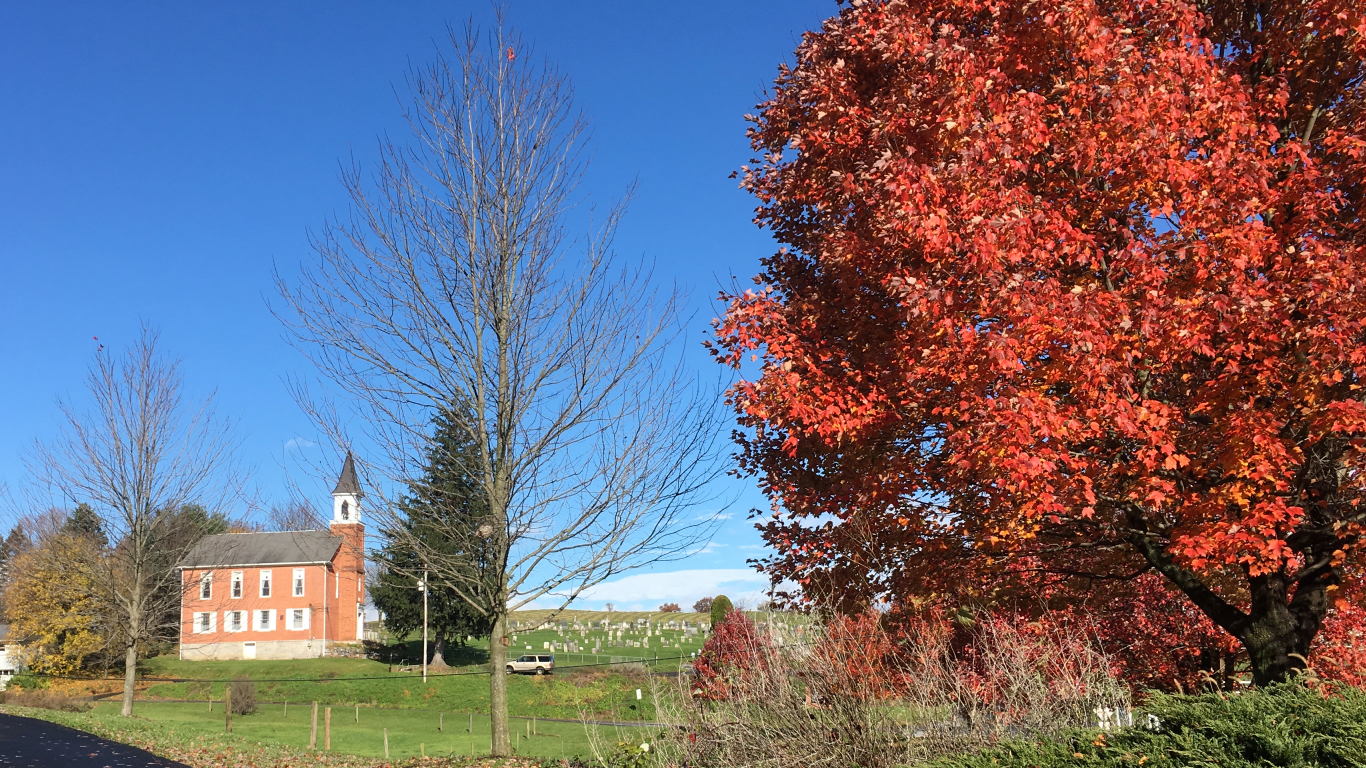 left to right: tall
              brick old country church, cemetery on a hill, red fall
              foliage on a tree
