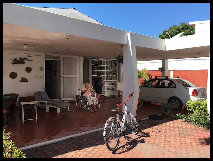 color photo of back patio at Pacific beach
                house, elderly woman in wheel chair