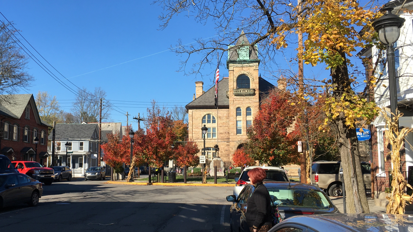 small square surrounded by
                neat houses except on the far side an official building
                with big windows and tower and flag