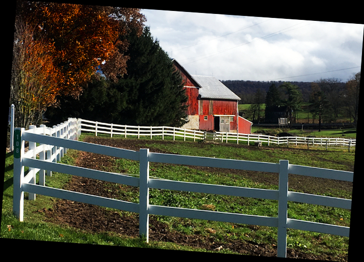 typical neat and tidy
              Pennsylvania red barn with white fences and cloudy sky and
              fall colors in trees
